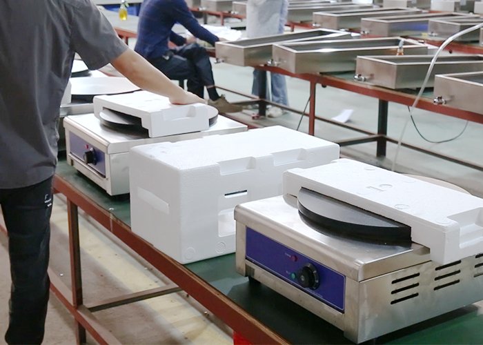 Worker packing commercial electric crepe makers with protective foam at the Tarzan Kitchen factory